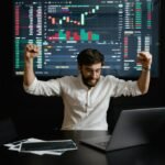 Happy trader celebrates profit in front of laptop and stock charts – myfastbroker stock brokers