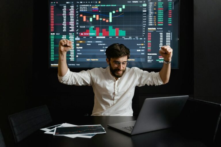Happy trader celebrates profit in front of laptop and stock charts – myfastbroker stock brokers