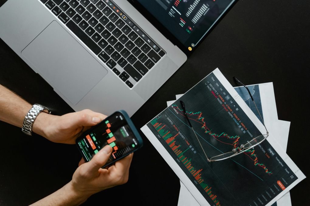 Investor using mobile trading app with stock charts and laptop – myfastbroker stock brokers