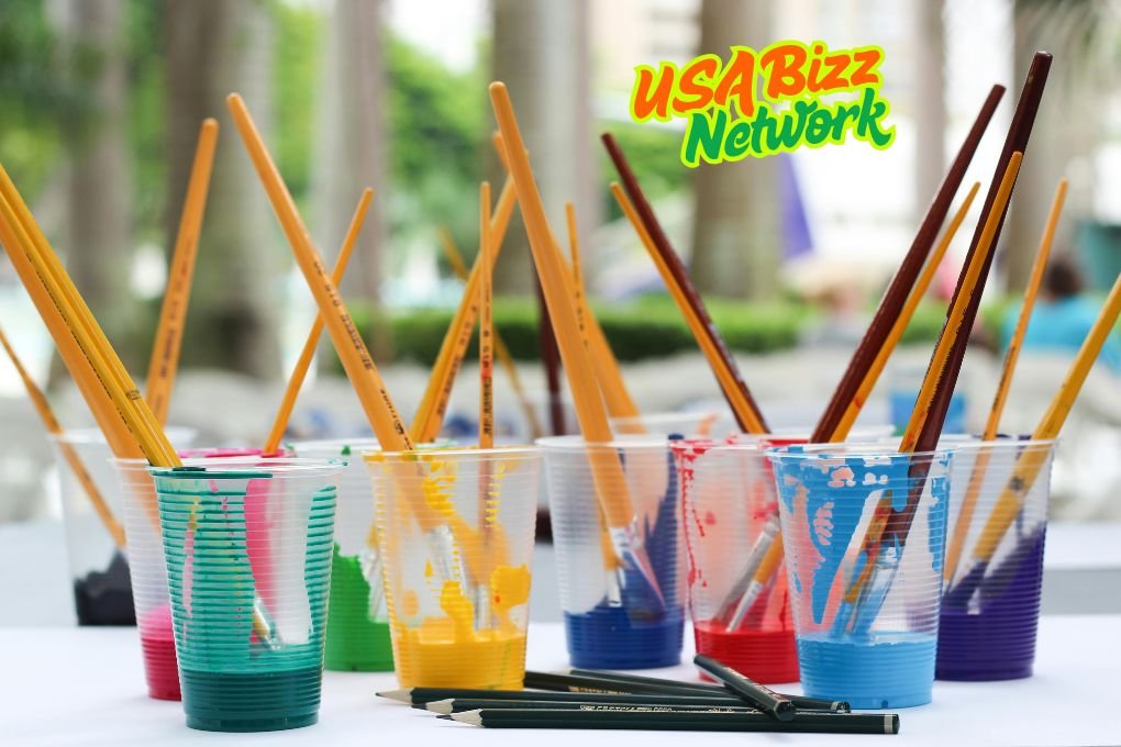 Art brushes in a yellow cup with colorful fruits in the background – Artofzio creative workspace